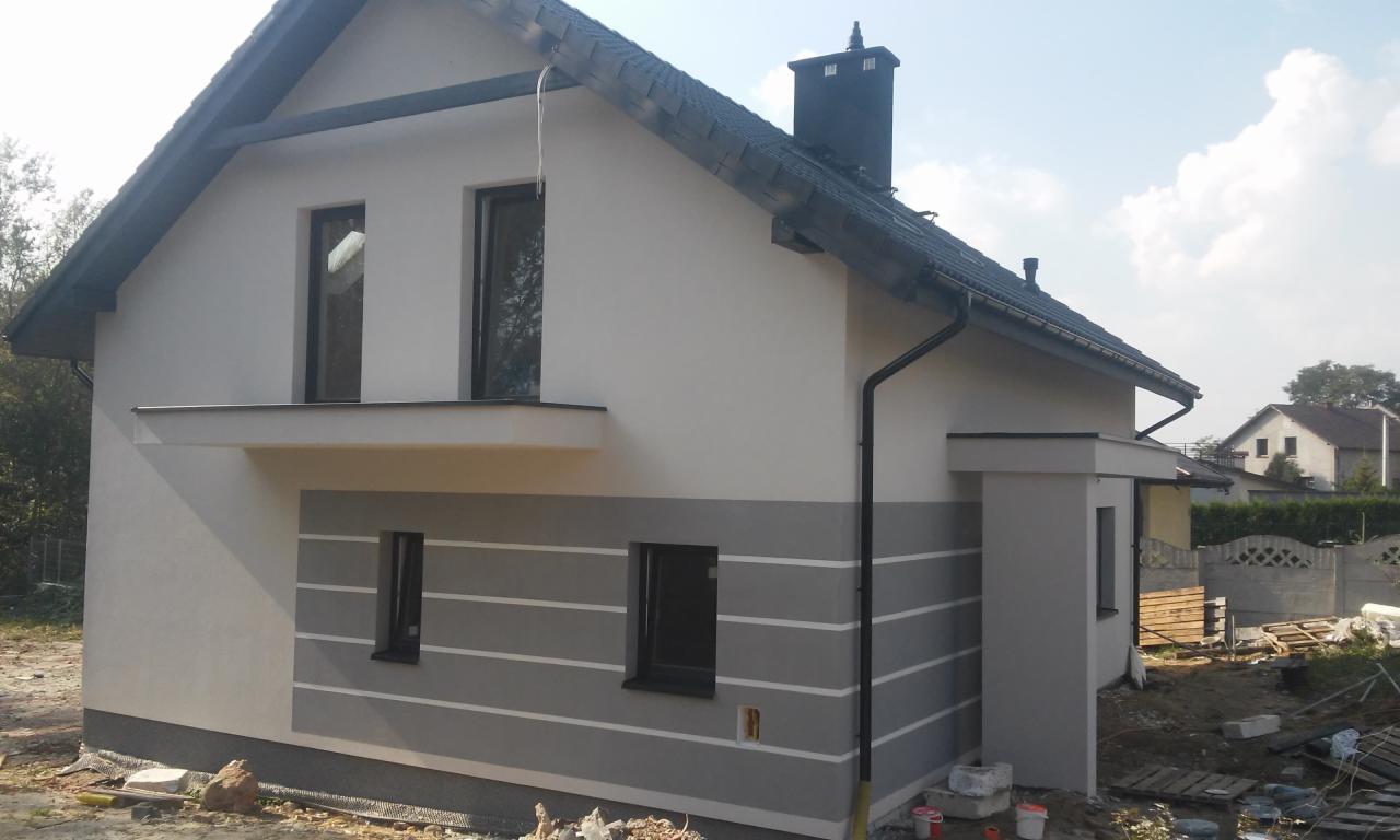 Świeżo wykończony dom jednorodzinny z szarą elewacją w poziome pasy, z czarną dachówką i orynnowaniem, widok z zewnątrz na tle nieba i sąsiednich zabudowań.