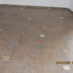 Beżowa podłoga z nieregularnych płytek, urozmaicona kolorowymi akcentami w postaci małych kwadratów. Widoczna data wykonania zdjęcia w prawym dolnym rogu.