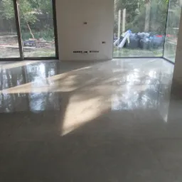 Błyszcząca, szara posadzka w pomieszczeniu z dużymi oknami w Ząbkach, odbijająca światło słoneczne i widok na zewnątrz.