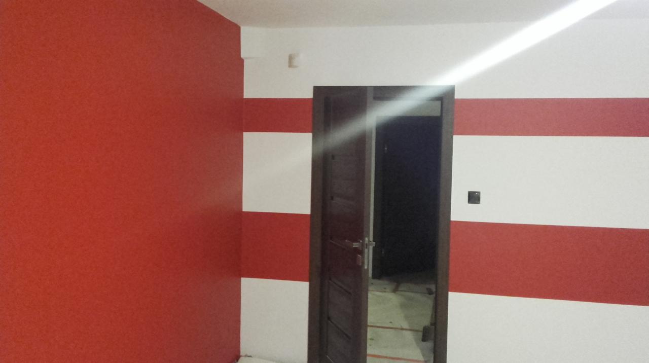 Pomieszczenie po malowaniu z poziomymi pasami czerwieni i bieli na ścianie, z otwartymi drewnianymi drzwiami i czerwoną ścianą po lewej stronie.