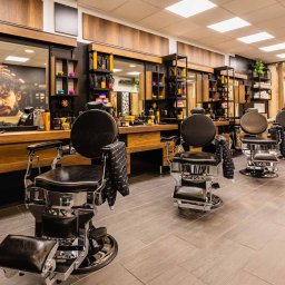 Projektownia - Nowoczesne wnętrze barber shopu z czterema skórzanymi fotelami fryzjerskimi, drewnianymi elementami wystroju i lustrami z kosmetykami. Stonowana kolorystyka.