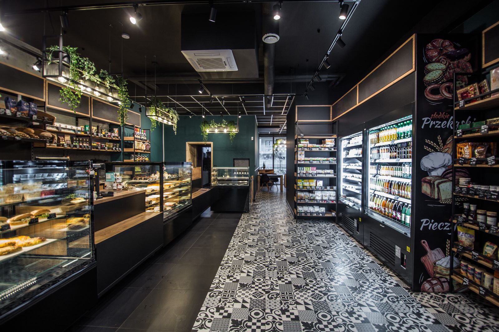 Nowoczesna aranżacja wnętrza sklepu spożywczego z czarnym sufitem, wzorzystą podłogą i ekspozycją produktów w chłodniach oraz na półkach.