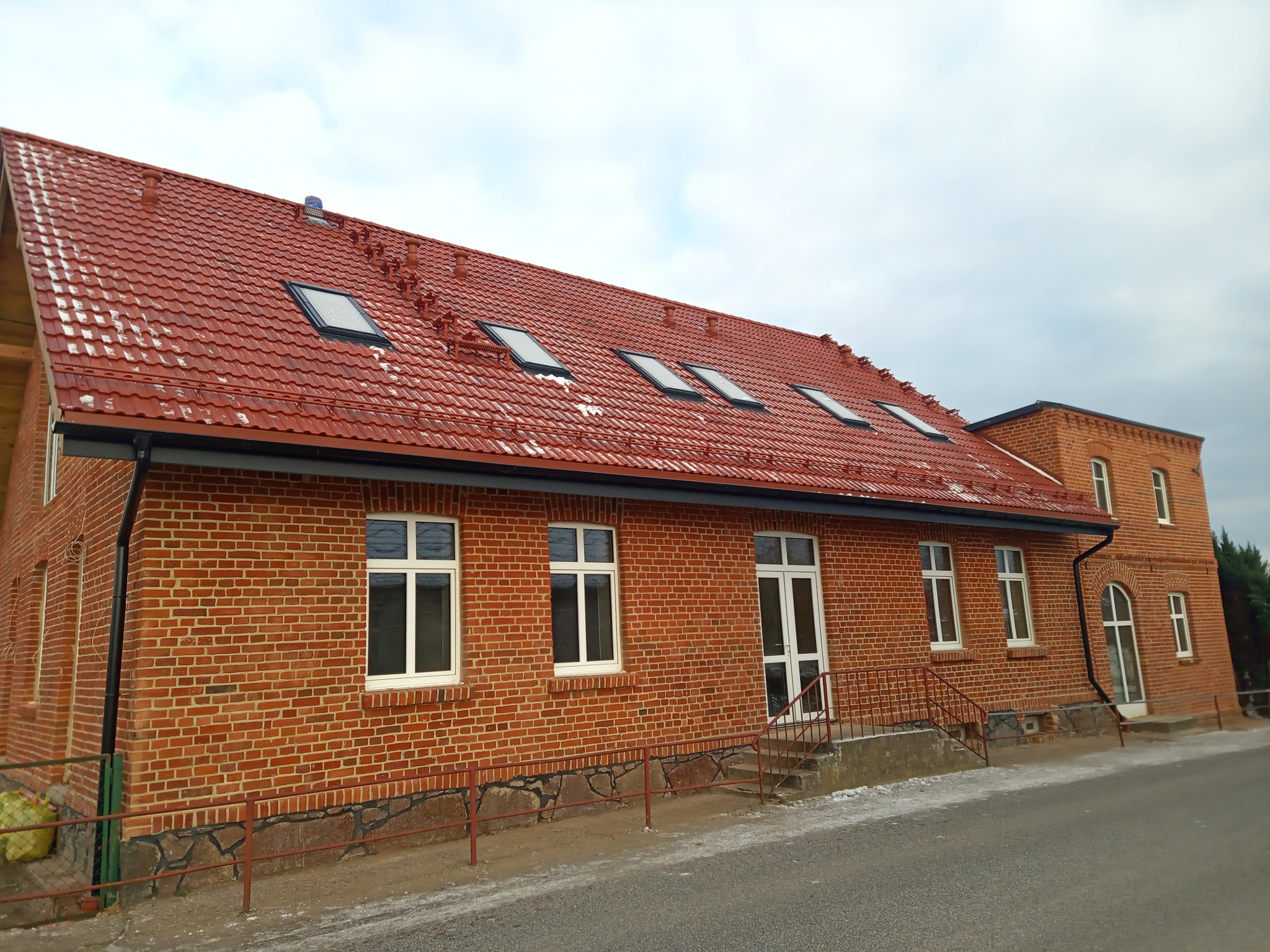 Dwukondygnacyjny budynek z czerwonej cegły z nowym, czerwonym dachem ceramicznym z oknami dachowymi i białymi ramami okiennymi.