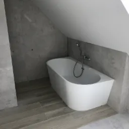 Nowoczesna łazienka na poddaszu z białą wanną wolnostojącą, szarą glazurą imitującą beton i drewnopodobną podłogą z płytek.