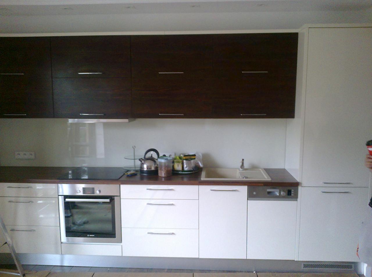 Nowoczesna kuchnia z brązowymi szafkami górnymi i białymi dolnymi. Widoczny piekarnik, zlew i akcesoria kuchenne. Elementy ze stali nierdzewnej.