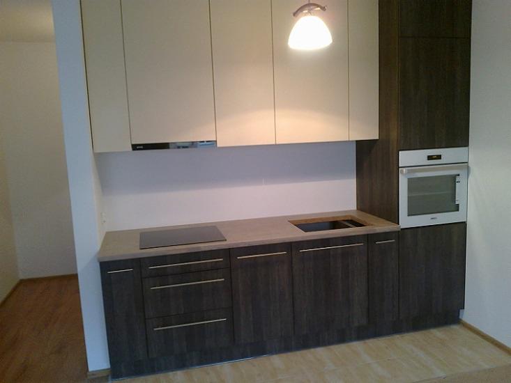 Nowoczesna kuchnia z brązowymi szafkami i beżowymi górnymi szafkami podświetlonymi lampą, płyta indukcyjna i piekarnik w zabudowie.