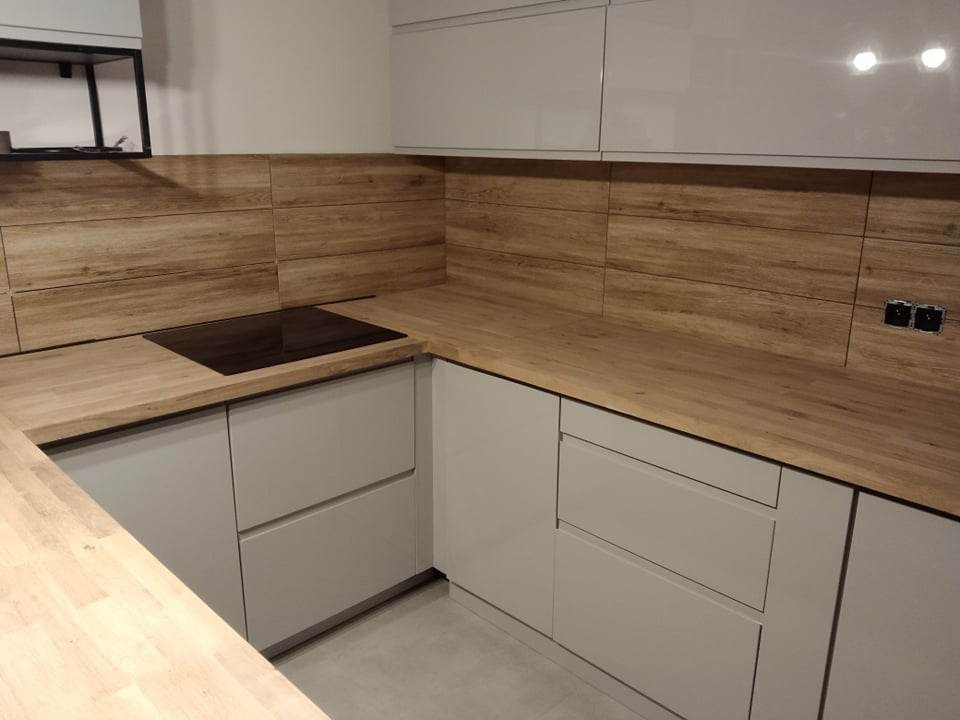 Nowoczesna kuchnia z drewnianymi panelami ściennymi i szarymi szafkami, minimalistyczny design, płyta indukcyjna wkomponowana w drewniany blat.