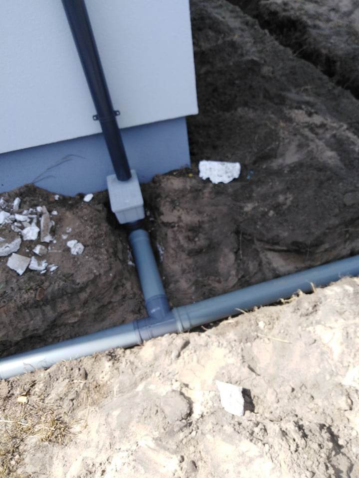 Szare rury kanalizacyjne łączone trójnikiem, częściowo zakopane w ziemi przy ścianie budynku w Częstochowie, widoczne fragmenty gruzu.