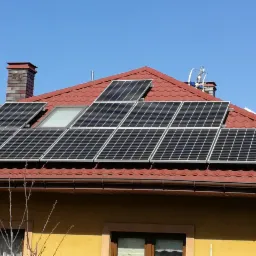 Czerwony dach domu z zamontowanymi panelami słonecznymi i oknem dachowym w słoneczny dzień.