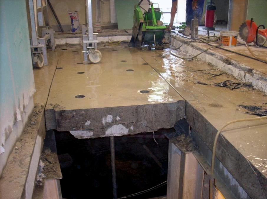 Cięcie betonu piłą diamentową, widoczne otwory w płycie betonowej i podpora konstrukcji. Prace budowlane wewnątrz budynku.