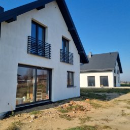 Firma Remontowo-Budowlana KAMBUD - Dwa nowoczesne domy z białymi elewacjami i ciemnymi dachami w słoneczny dzień. Widoczne okna z czarnymi ramami i metalowe balustrady balkonowe. Teren wokół w trakcie zagospodarowania.