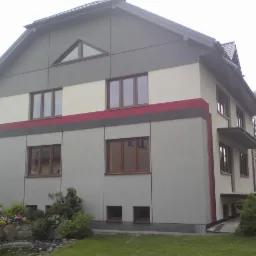 Dwupiętrowy dom z szarą elewacją, kremowym pasem i czerwonym akcentem, widok z ogrodu z oczkiem wodnym.