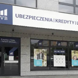 Fasada biura OVB z szyldem Ubezpieczenia, Kredyty, Leasingi oraz plakatami w oknach: seniorzy z psem i dziecko, informacja o OC/AC/NNW.