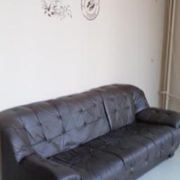 AMT SERWIS - Ciemnobrązowa skórzana sofa z pikowaniem na tle ściany z naklejkami 'Coffee Káva' i symbolem espresso. Widok z perspektywy.