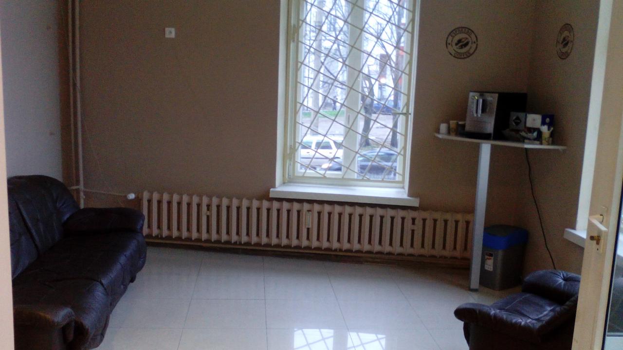 Pokój poczekalni z ciemną sofą, fotelem, grzejnikiem pod oknem z kratą i stolikiem z ekspresem do kawy. Na ścianie dekoracyjne naklejki.