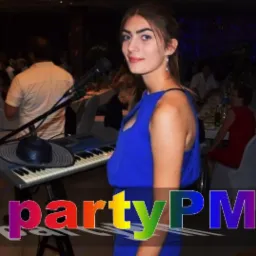 Piosenkarka w niebieskiej sukience stoi za keyboardem z mikrofonem i kapeluszem, w tle goście weselni.