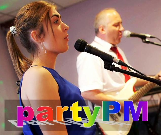 Zespół muzyczny podczas występu: wokalistka w niebieskiej sukience śpiewa do mikrofonu, gitarzysta w tle gra na białej gitarze elektrycznej, widoczne logo 'partyPM' na pierwszym planie.