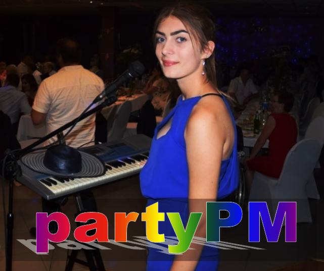 Piosenkarka w niebieskiej sukience stoi za keyboardem z mikrofonem i kapeluszem, w tle goście weselni.