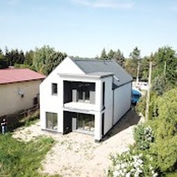 WESKAD-BUD Budownictwo - Nowoczesny, dwukondygnacyjny budynek z płaskim dachem, białymi ścianami i dużymi oknami, widziany z lotu ptaka, otoczony zielenią i innymi budynkami.