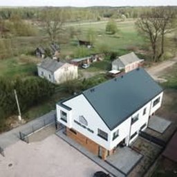 WESKAD-BUD Budownictwo - Nowoczesny, dwukondygnacyjny dom z białymi ścianami i grafitowym dachem, widziany z lotu ptaka na tle zielonego terenu. Minimalistyczna architektura, płaski dach.