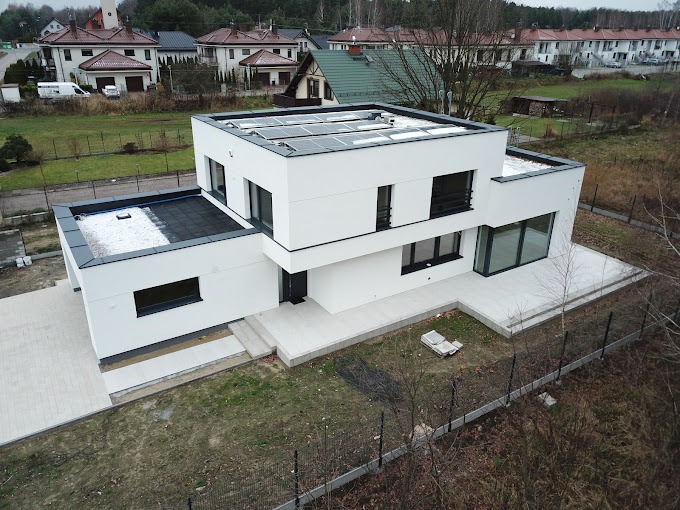 Nowoczesny, dwukondygnacyjny dom z płaskim dachem i panelami słonecznymi, widok z góry na wykończony teren wokół budynku.