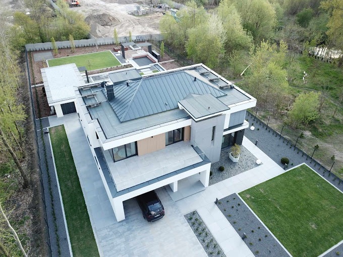 Nowoczesny, dwukondygnacyjny dom z płaskim dachem, widok z drona, z garażem na samochód i zadbanym ogrodem z trawnikiem i szarym żwirem.