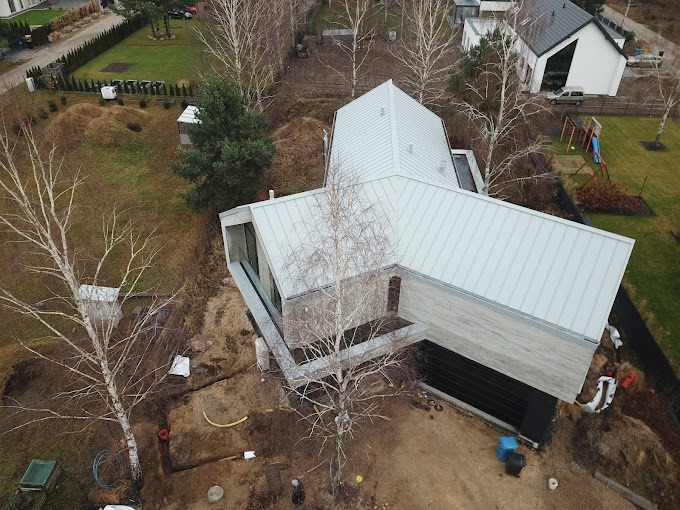 Nowoczesny dom z szarą blachą na dachu, widok z góry na plac budowy z wykopami pod instalacje.