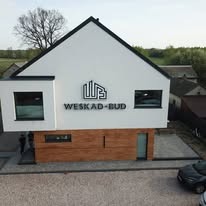 Nowoczesny dom z białymi ścianami i drewnianą elewacją, z logo firmy WESKAD-BUD. Widok z góry, boczny, z widocznym fragmentem otoczenia i dwoma osobami.