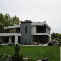 Nowoczesny dom z płaskim dachem, biało-szara elewacja z elementami drewna. Duże okna, zadbany trawnik, widok z poziomu gruntu. Minimalistyczny design.