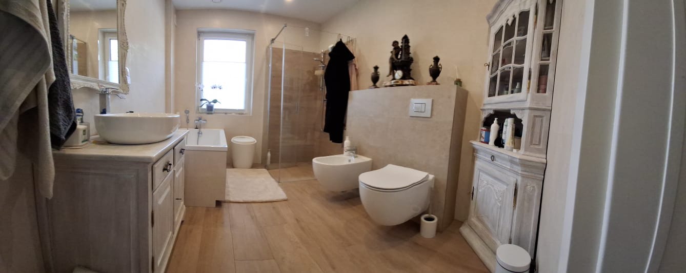 Jasna łazienka z drewnopodobnymi płytkami, kabiną prysznicową typu walk-in, wiszącą miską WC i bidetem oraz szafką pod umywalkę w stylu shabby chic.