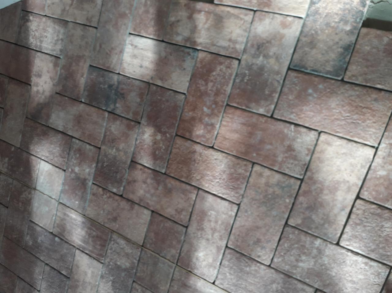 Ukończona ściana z dekoracyjnej cegły w odcieniach brązu, ułożonej w jodełkę. Widoczne nierówności faktury i delikatne refleksy światła.