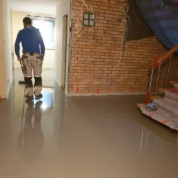 Wylewka jastrychowa w trakcie rozprowadzania w pomieszczeniu z zabezpieczonymi ścianami z cegły i schodami, widoczny pracownik z narzędziem.