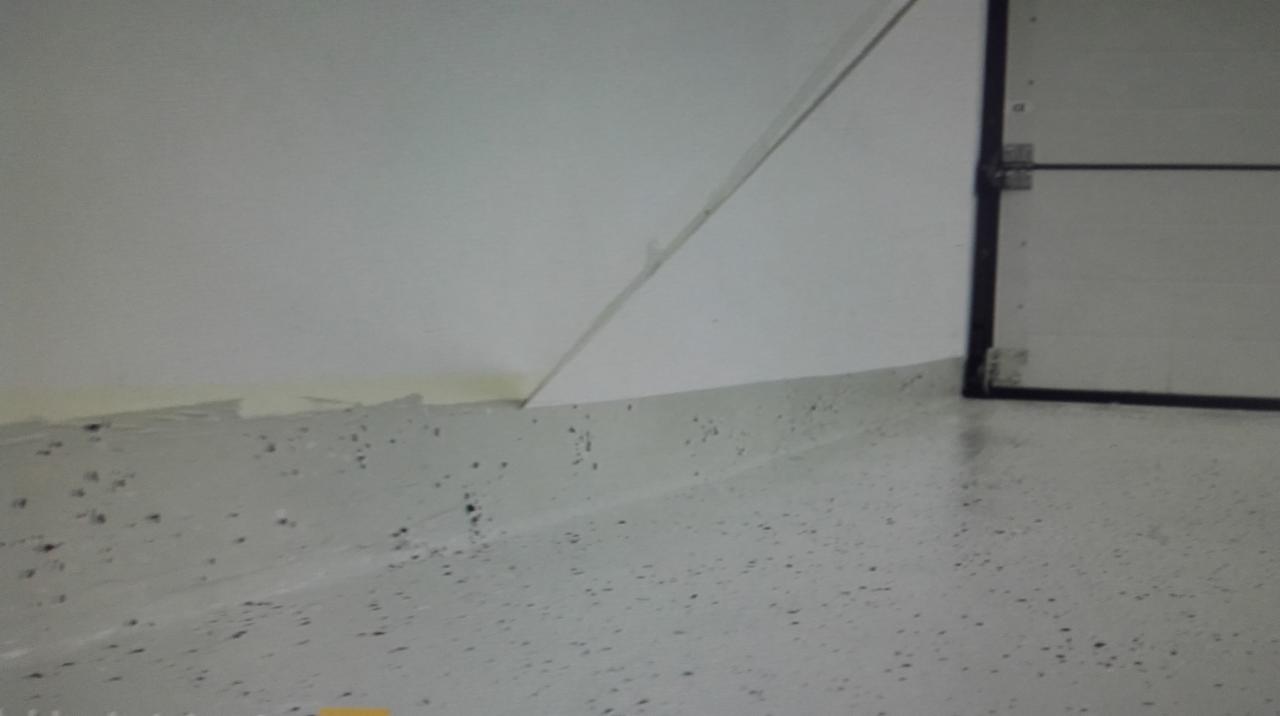 Jasnoszara, wykończona posadzka z drobnymi, ciemnymi plamkami, łącząca się ze ścianą i fragmentem czarnej ramy drzwi.