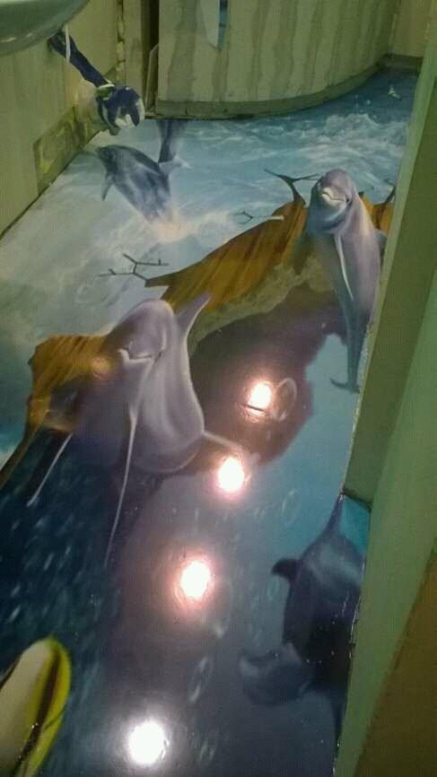 Żywiczna posadzka z trójwymiarowym motywem delfinów w wodzie, z efektem głębi i odbiciami światła, z fragmentem umywalki w tle.