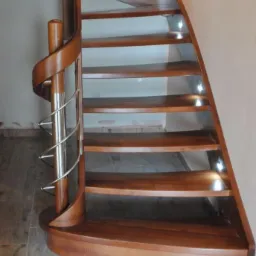 Kręte schody drewniane z oświetleniem punktowym pod stopniami i metalową balustradą.