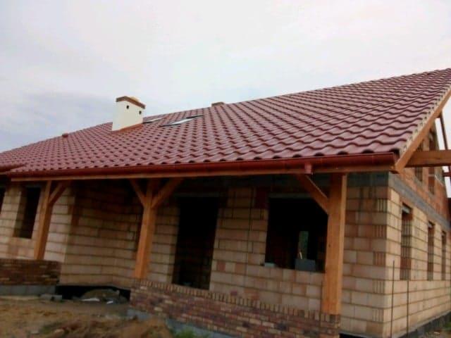 Budowa domu z czerwonym dachem w Budzisławiu Kościelnym, widoczne drewniane elementy konstrukcyjne i ceglane ściany w trakcie wznoszenia.