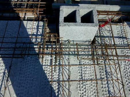 Wznoszenie ściany z bloczków betonowych zbrojonych stalą, widok z góry na szary beton komórkowy i siatkę z prętów żebrowanych.