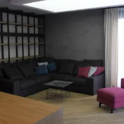 Nowoczesny salon z narożną sofą, metalowym regałem na książki, fuksjowym fotelem z podnóżkiem i drewnianą podłogą w jodełkę.