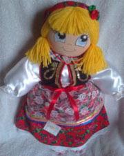 Ręcznie szyta lalka w stroju ludowym, z blond włosami i czerwoną chustą. Detale stroju: haftowany gorset, wzorzysta spódnica. Idealna jako pamiątka regionalna.