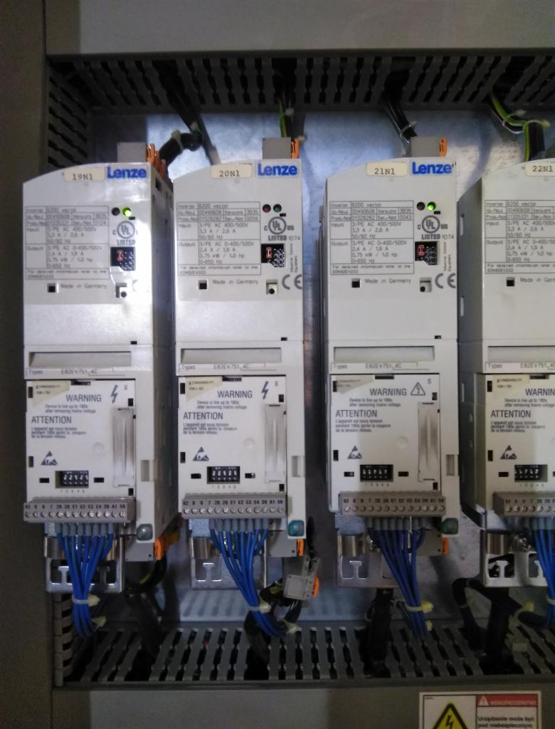 Cztery identyczne falowniki Lenze zamontowane w szafie sterowniczej, z widocznymi podłączeniami kablowymi w kolorze niebieskim i zielonymi diodami LED sygnalizującymi pracę.