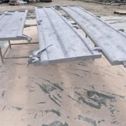 Metalowe elementy konstrukcyjne po obróbce, leżące na zabezpieczonej powierzchni z widocznymi śladami procesu. Elementy są szare, matowe i ułożone równolegle.