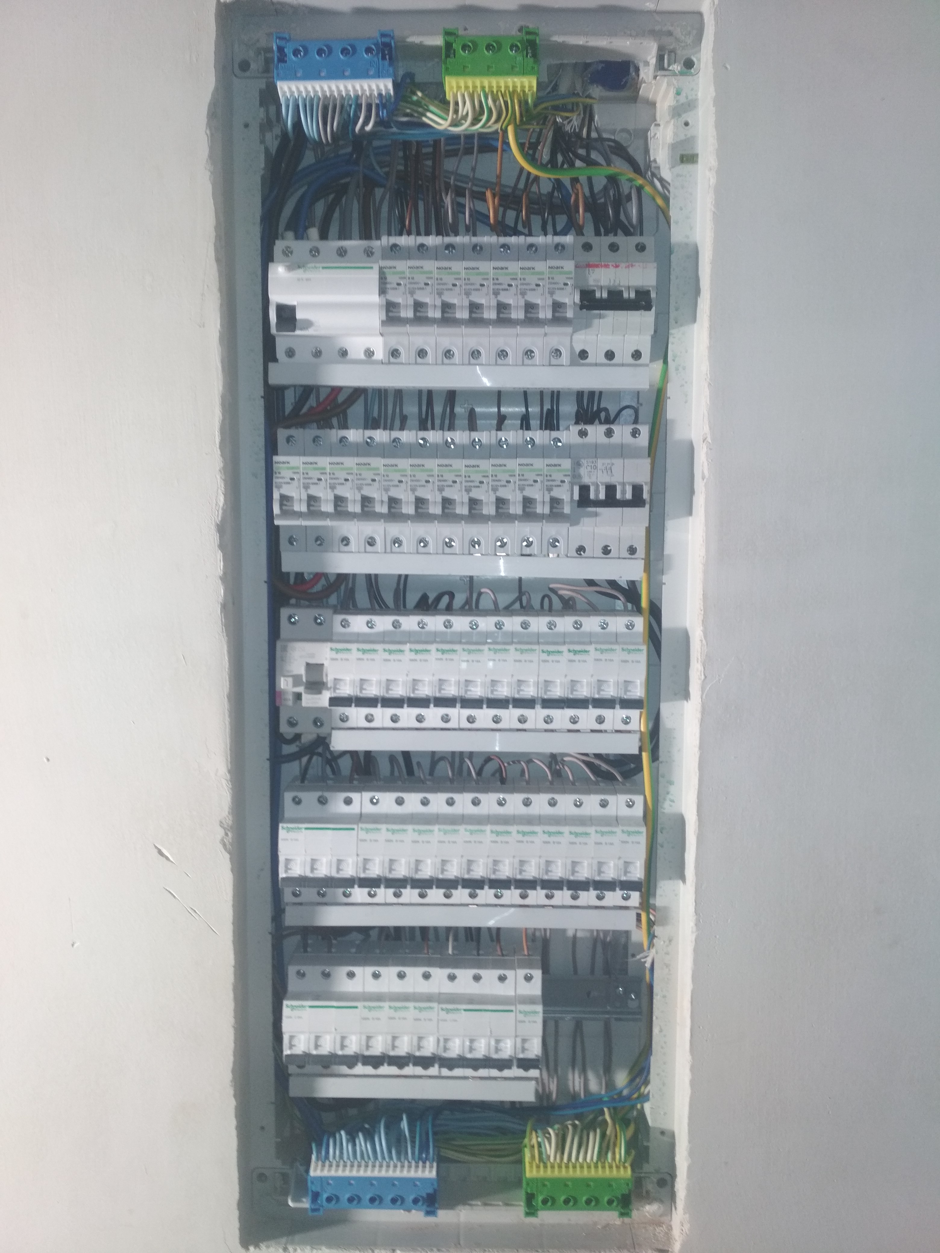 Rozdzielnia elektryczna wnękowa z zamontowanymi bezpiecznikami i podłączonymi przewodami. Widoczne listwy zaciskowe i wyłączniki nadprądowe.