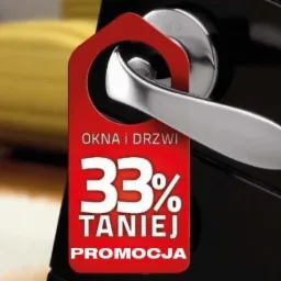 Klamka drzwi z zawieszką reklamową: 'Okna i drzwi 33% taniej PROMOCJA'. Zawieszka czerwona, na czarnym tle. Chromowana klamka. Widoczny fragment żółtej sofy.