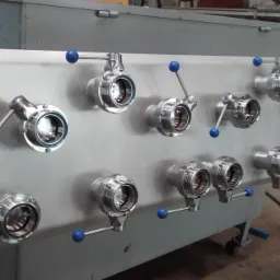 Panel z zamontowanymi, metalowymi zaworami motylkowymi z niebieskimi uchwytami, widoczne gwinty i elementy konstrukcyjne.