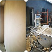 Świeżo nałożony tynk na ścianie wewnętrznej pomieszczenia, widoczna maszyna tynkarska z mieszadłem i pompą, częściowo na zewnątrz budynku, z rusztowaniem w tle.