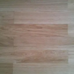 Jasne, dębowe panele podłogowe ułożone w regularny wzór. Widoczne delikatne usłojenie drewna i subtelne różnice w odcieniach poszczególnych desek.