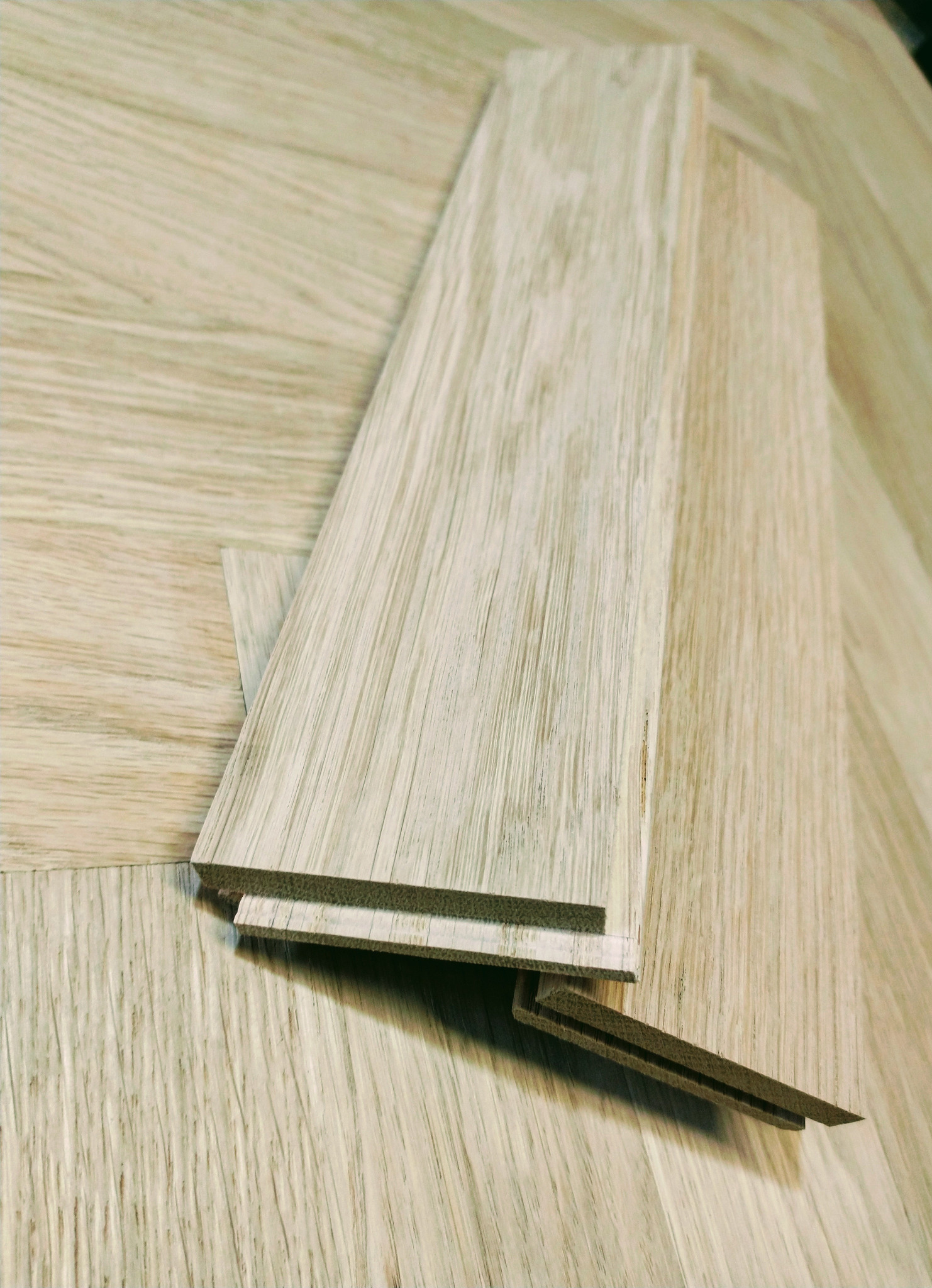 Jasne panele podłogowe z widocznym systemem łączenia, ułożone na podłożu imitującym drewno. Prezentacja produktu z bliska, ukazująca strukturę i detale.