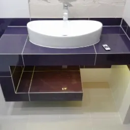 Biała umywalka nablatowa na ciemnofioletowym blacie z płytek, wykończona z podświetleniem. Widoczny fragment toalety i pilot. Nowoczesna aranżacja łazienki.