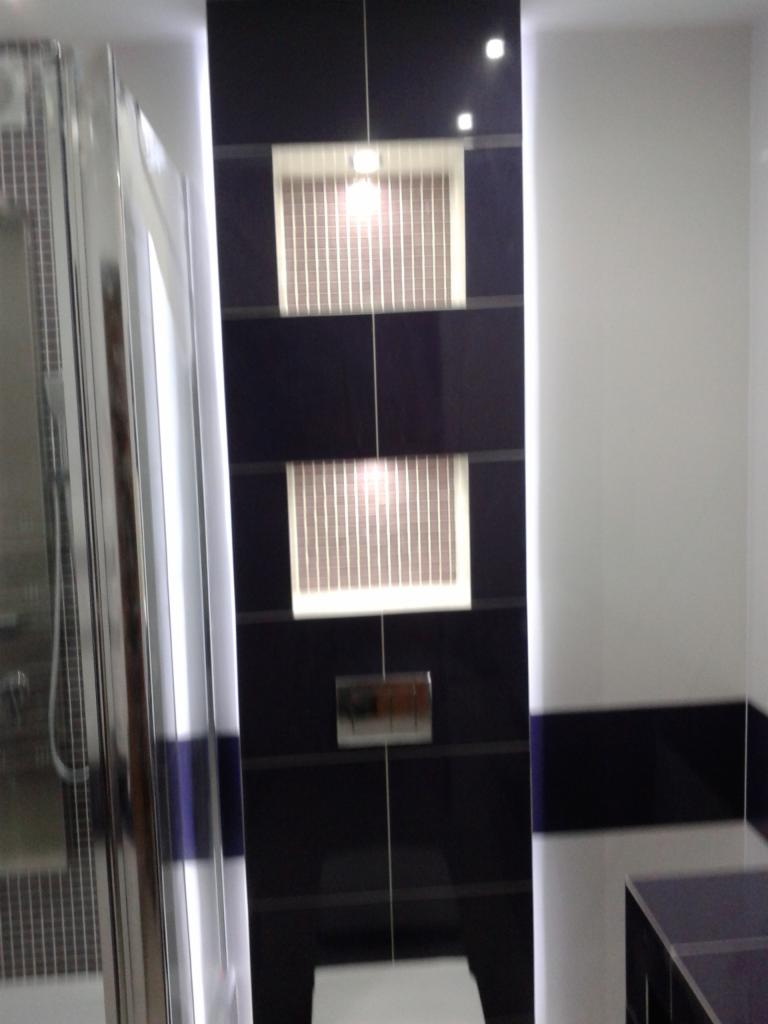 Nowoczesna łazienka z czarnymi, błyszczącymi płytkami, dwoma białymi kratkami wentylacyjnymi i kabiną prysznicową z chromowanymi detalami.