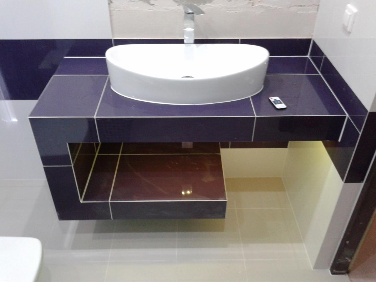 Biała umywalka nablatowa na ciemnofioletowym blacie z płytek, wykończona z podświetleniem. Widoczny fragment toalety i pilot. Nowoczesna aranżacja łazienki.